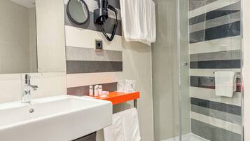 A modern bathroom with a white sink, a hairdryer, a mirror, and a shower area.