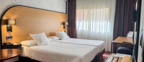 A hotel room with two beds, a desk, a chair, and a small table.