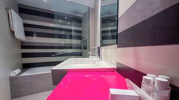 Un baño moderno con un espejo grande, una ducha con cerramiento de vidrio y un tocador rosa con artículos de aseo.