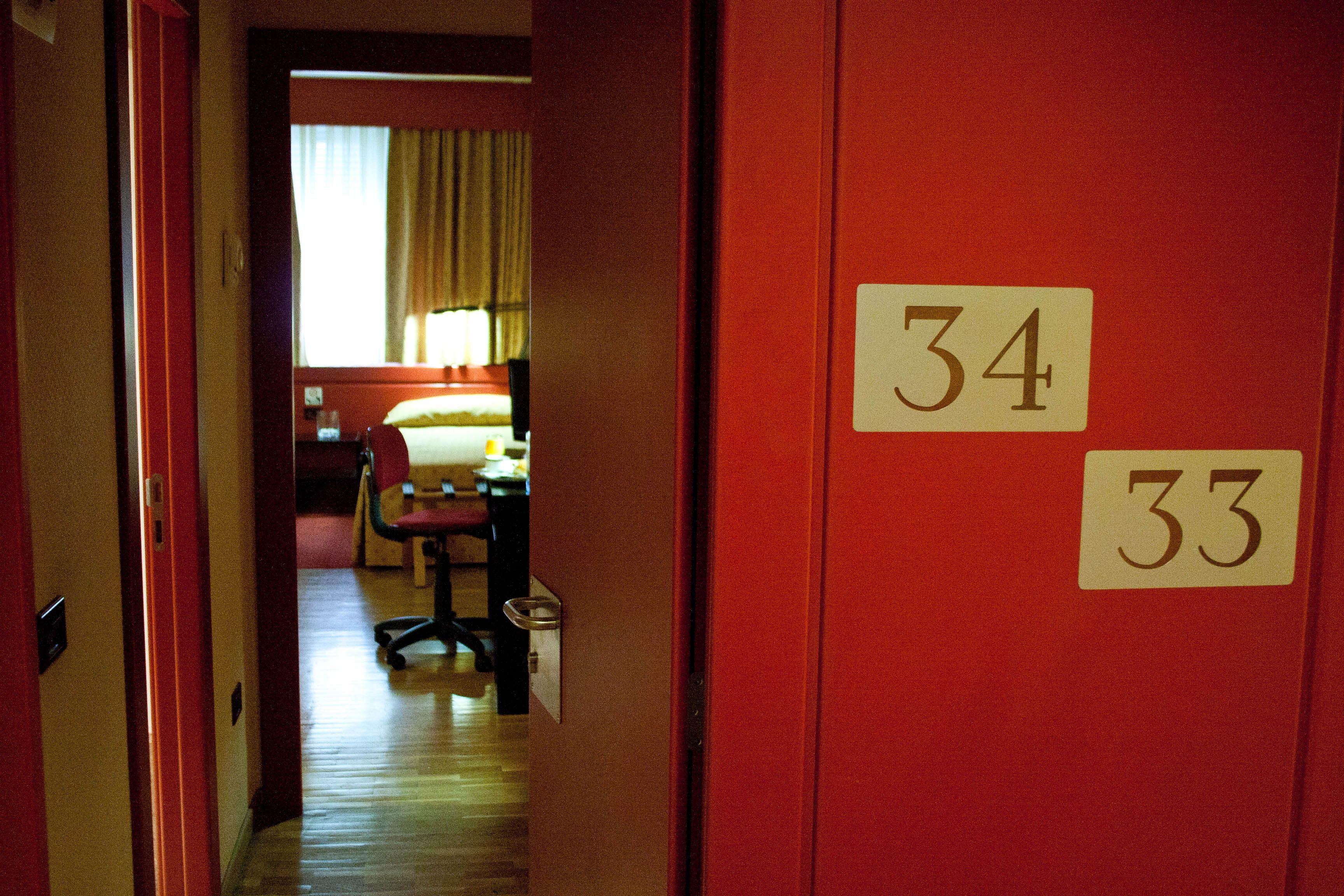 A hotel room with a wooden floor, a bed with a white comforter, a chair, and a desk. The room number is 34.