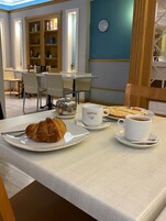 Una mesa de comedor con croissants, una taza de café y un plato de comida en un entorno hotelero.