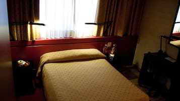Habitación de hotel con cama, mesita de noche, lámpara y ventana con cortinas.