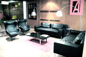 Una sala de estar moderna con un sofá de cuero negro, dos sillones negros, una mesa de centro de vidrio y una alfombra rosa.