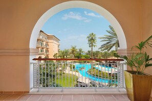 A balcony with a view of a swimming pool, palm trees, and a building with balconies.