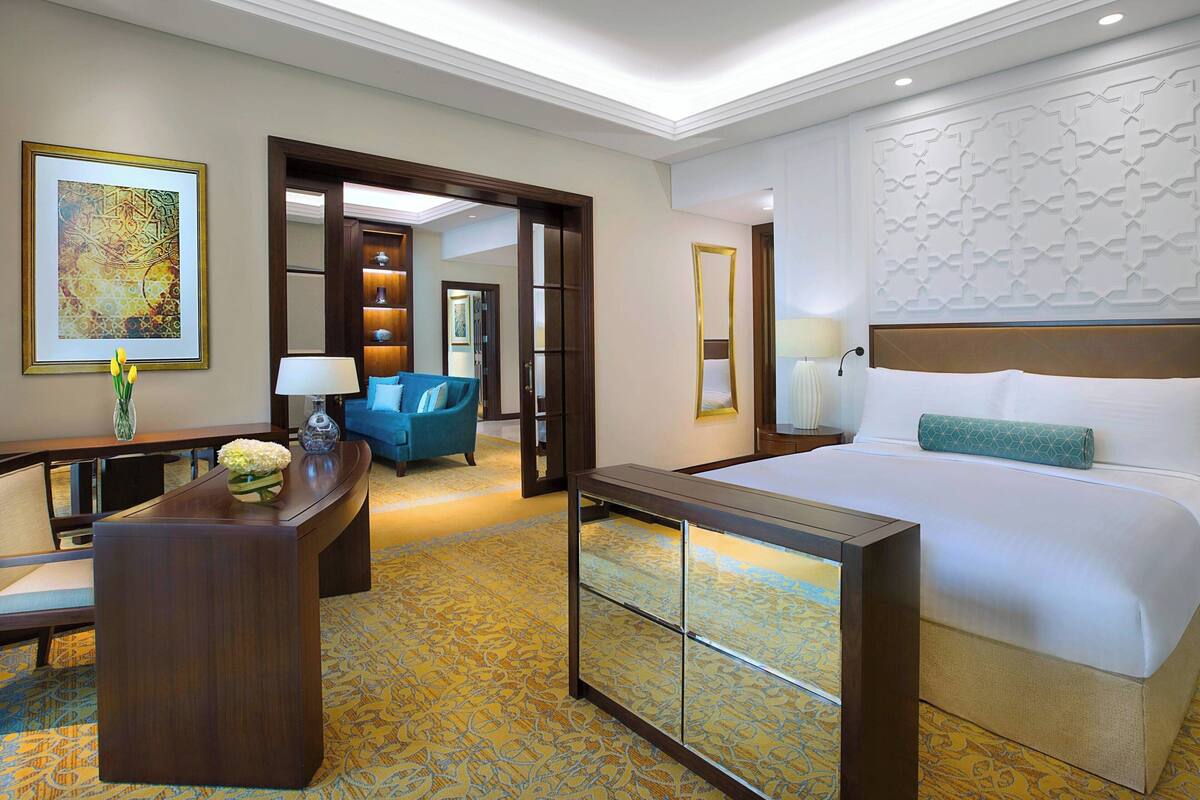 A hotel room with a large bed, a desk with a lamp, a chair, and a decorative wall piece.