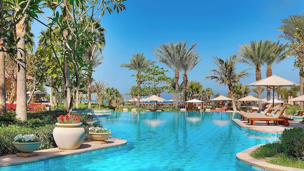 A swimming pool with lounge chairs and umbrellas, surrounded by palm trees and potted plants.