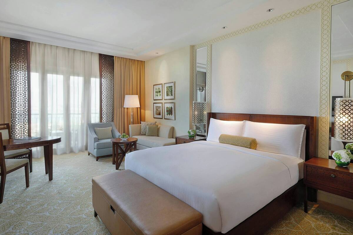 A hotel room with a large bed, a desk, a chair, a sofa, and a small table.