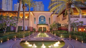 A hotel courtyard with a central fountain, palm trees, and a large arched entrance.