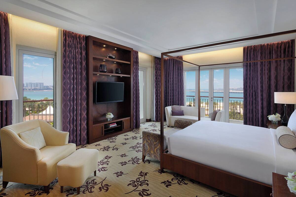 A hotel room with a large bed, a sofa, a TV, and a balcony with a view.