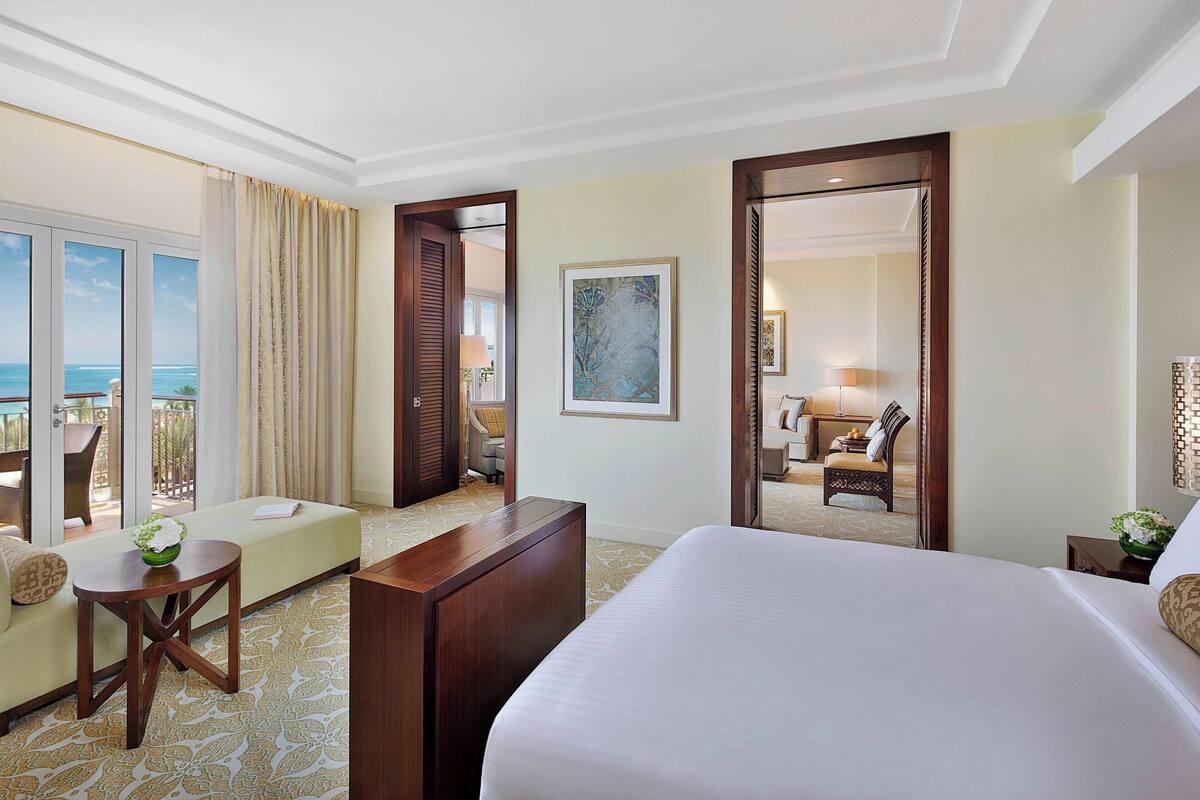 A hotel room with a large bed, a sofa, a desk, and a view of the ocean through large windows.