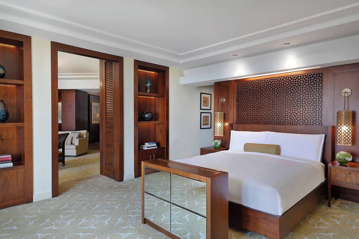A hotel room with a large bed, wooden headboard, a bedside table with a lamp, and a decorative wall panel.