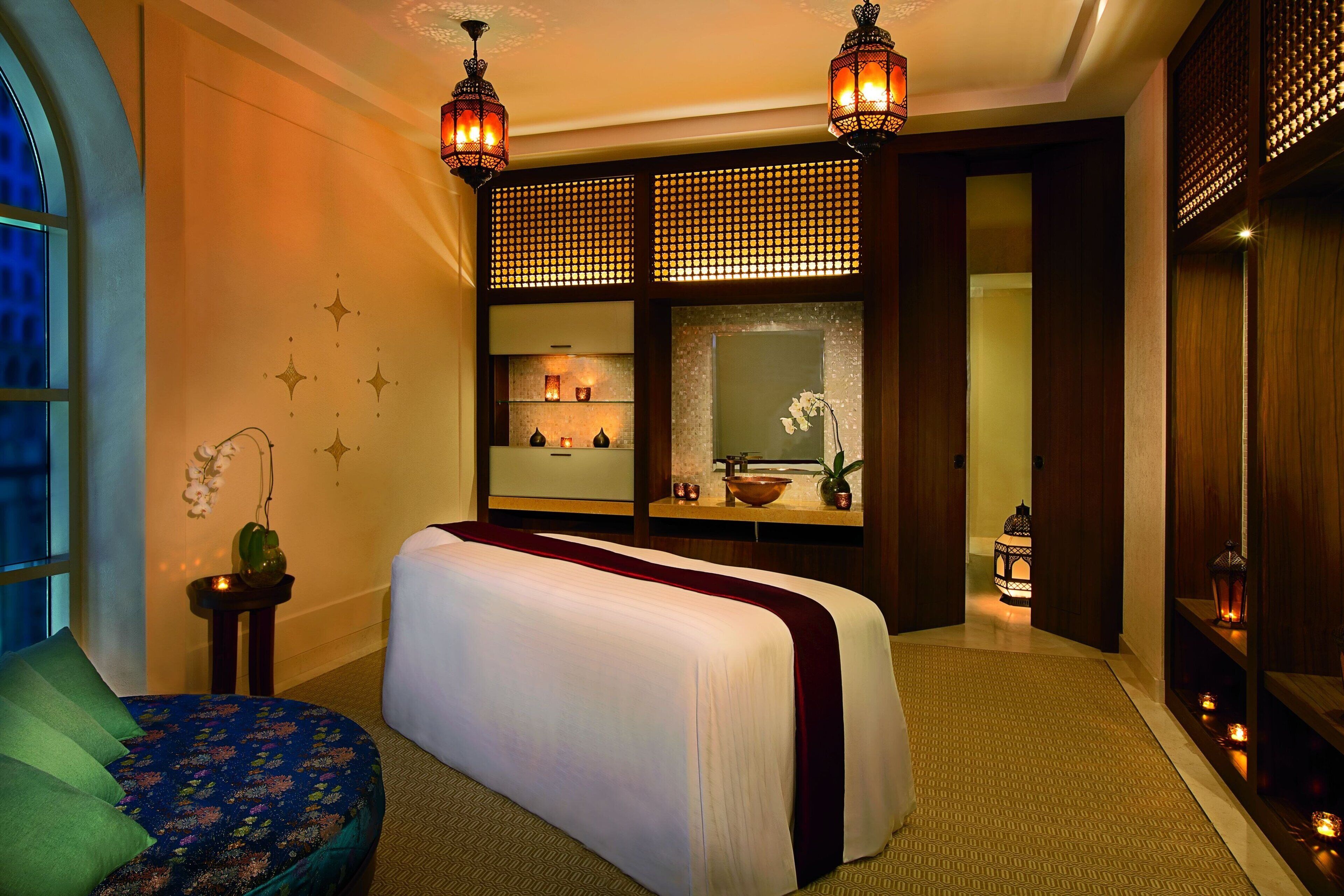 A hotel room with a large bed, a small seating area, a vanity with a mirror, and decorative lighting.