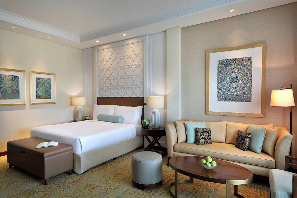 A hotel room with a bed, a sofa, a coffee table, a side table, and a lamp.