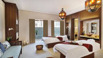 A hotel room with two beds, a sitting area, a large window, and a bathroom with a mirror and sink.