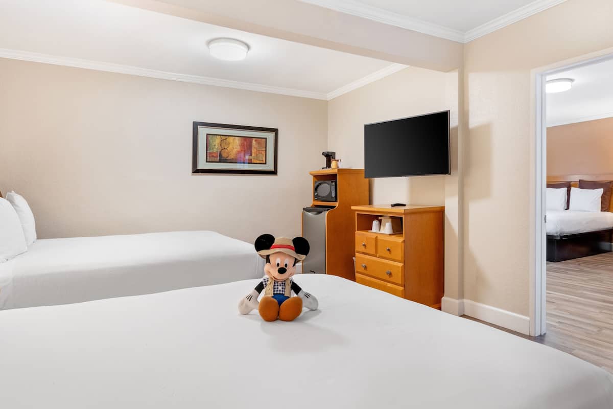 A hotel room with two beds, a television, a painting on the wall, and a Mickey Mouse plush toy on the bed.
