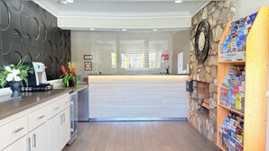 A reception area with a modern design, featuring a stone accent wall, a wooden bookshelf with brochures, and a counter with a coffee machine. - Anaheim Islander Inn and Suites (Anaheim)