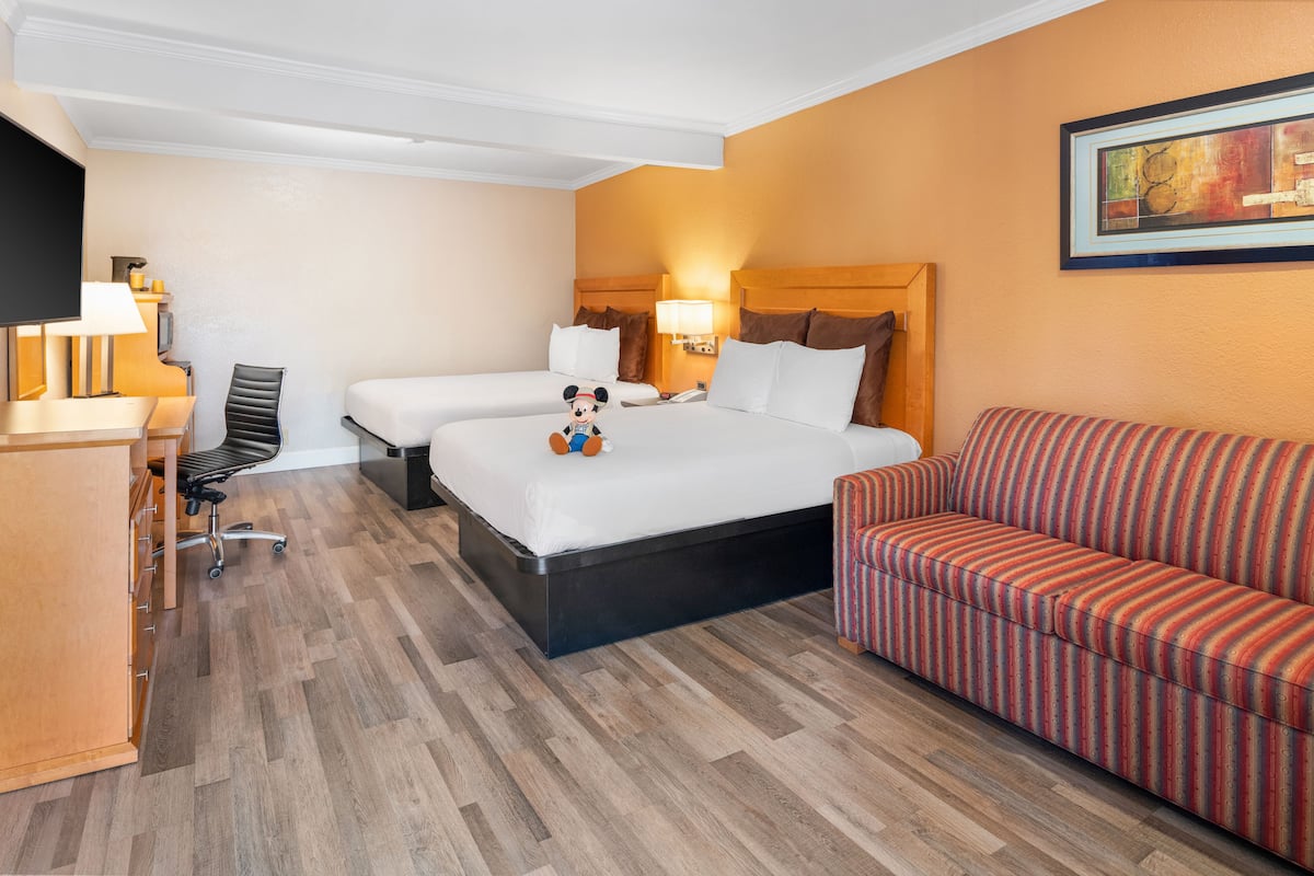 A hotel room with two beds, a desk, a chair, a sofa, and a TV.
