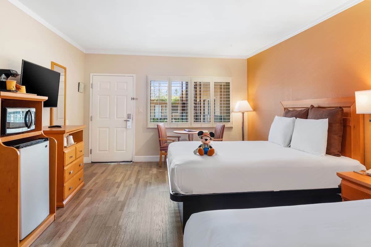 A hotel room with a bed, a desk with a computer, a television, and a Mickey Mouse plush toy.