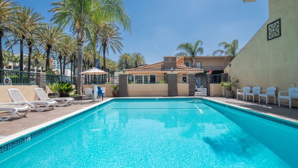 A swimming pool with lounge chairs, palm trees, and a building with a tiled roof. - Anaheim Islander Inn and Suites (Anaheim)