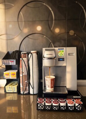 Une machine à café en train de verser du café dans une tasse, une pile de gobelets jetables et un plateau de dosettes de café.