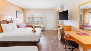 A hotel room with two beds, a desk, a chair, a TV, and a window with a view of greenery. - Anaheim Islander Inn and Suites (Anaheim)