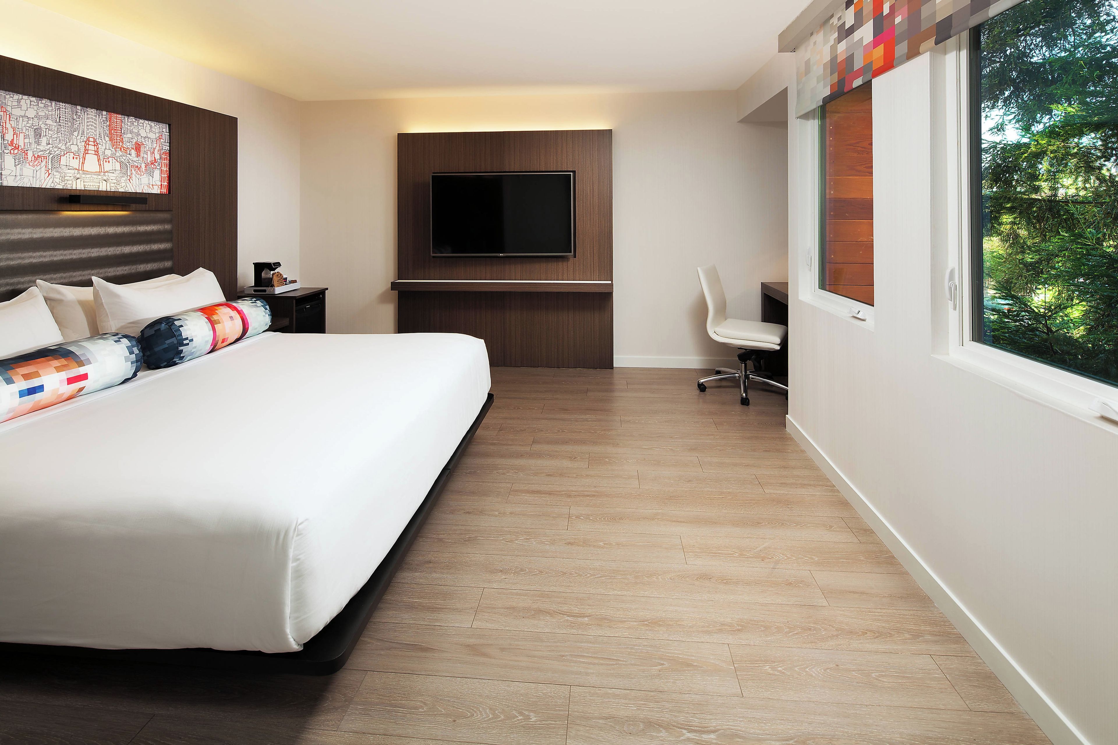 Een hotelkamer met een groot bed, een bureau met een flatscreen televisie en een raam met uitzicht op bomen.