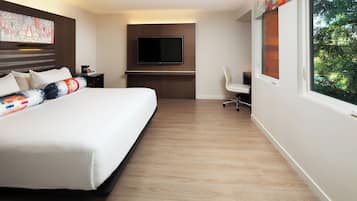 Habitación de hotel con una cama grande, un escritorio y un televisor de pantalla plana, y una ventana con vistas a árboles.
