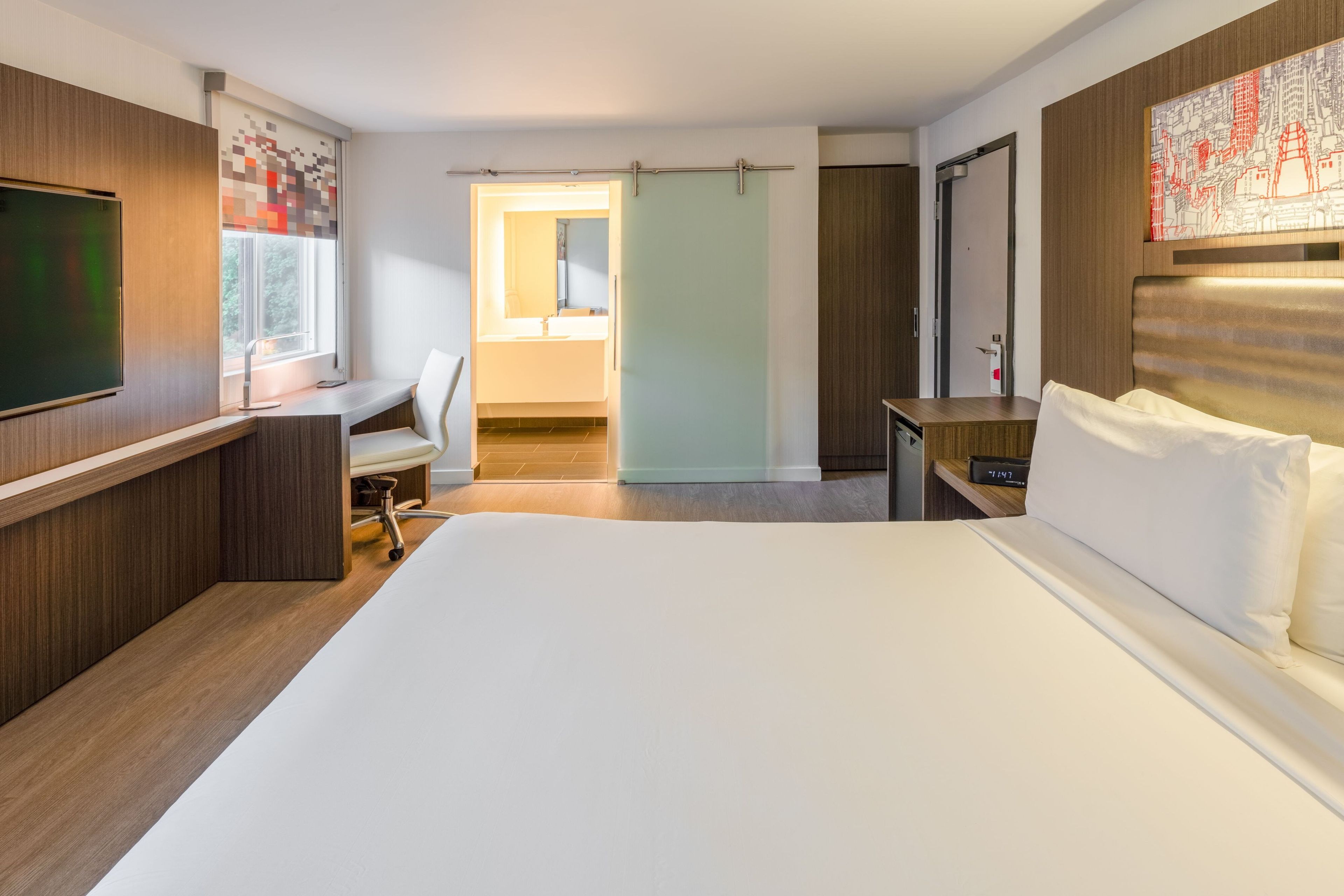 Habitació d'hotel amb llit, escriptori, cadira i televisió.