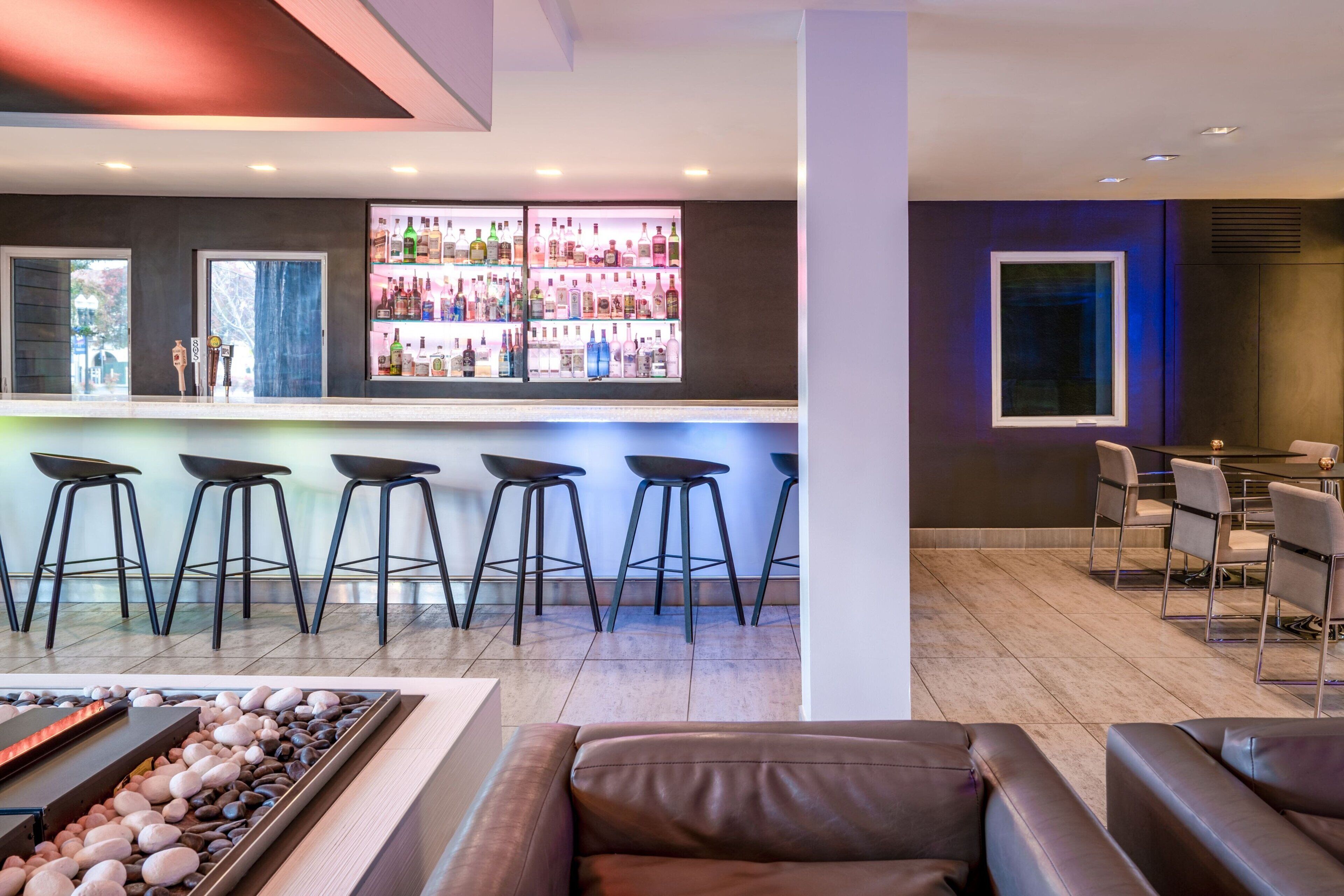A modern bar area with a long counter, multiple stools, and a seating area with a fire feature.