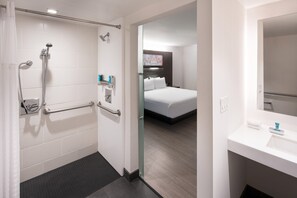 A hotel bathroom with a shower, grab bars, and a sink.