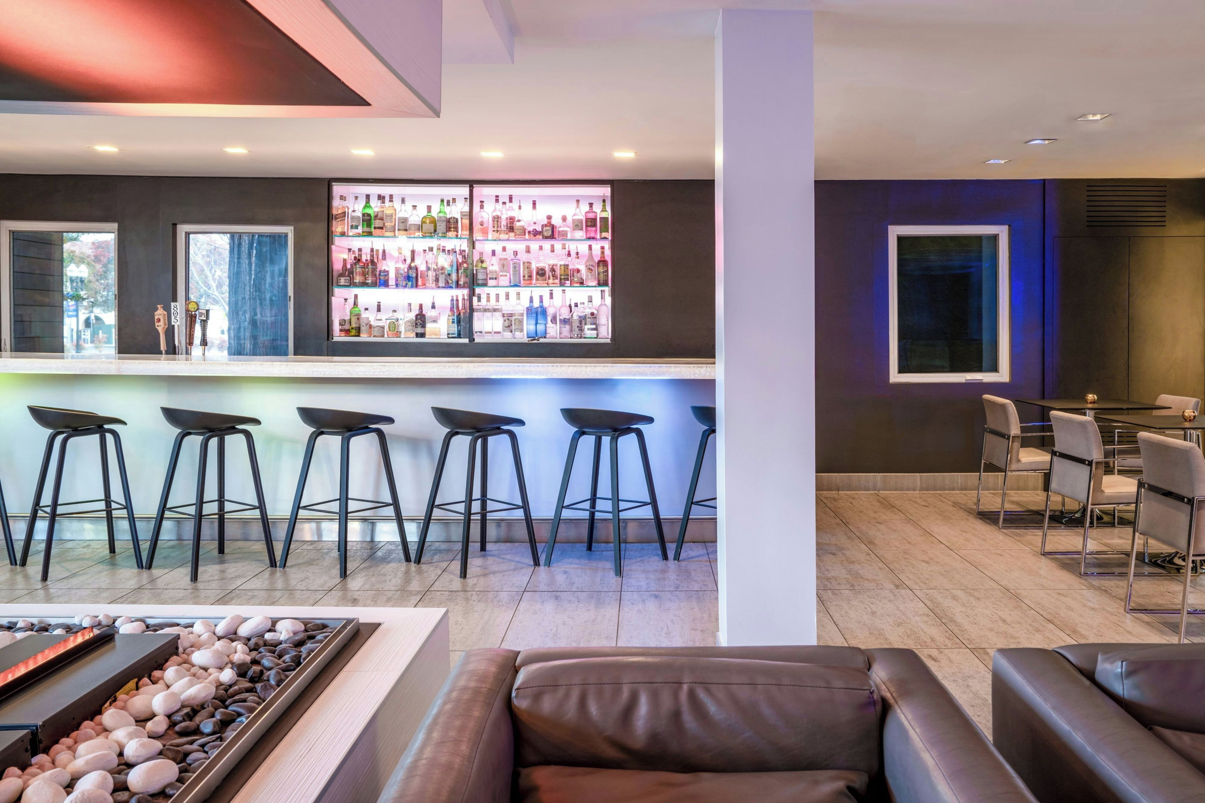 A bar area with stools and a bar counter stocked with bottles.
