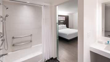 A modern bathroom with a bathtub, shower, and glass door leading to a bedroom.