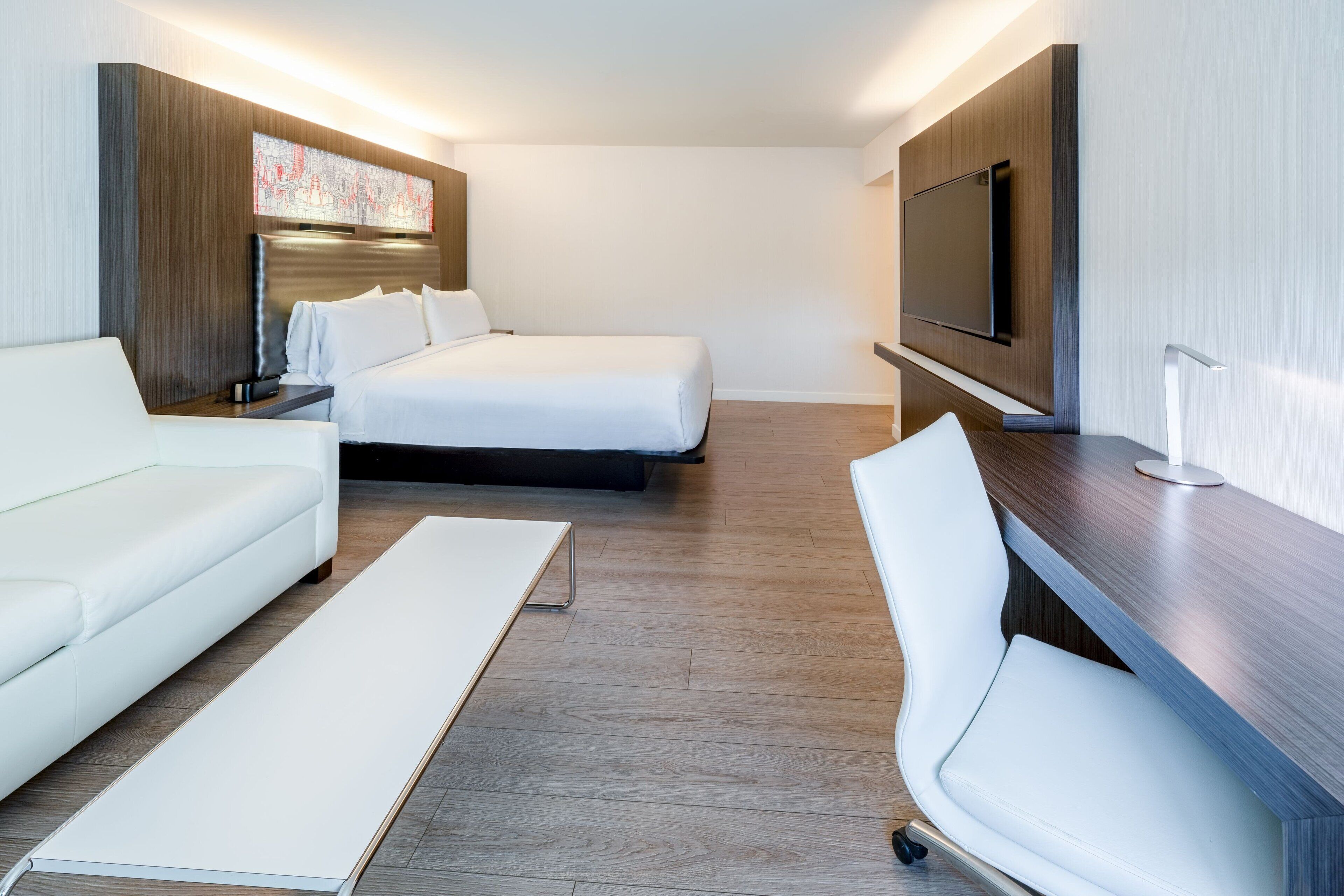 Una habitación de hotel moderna con cama, sofá, escritorio y televisión.