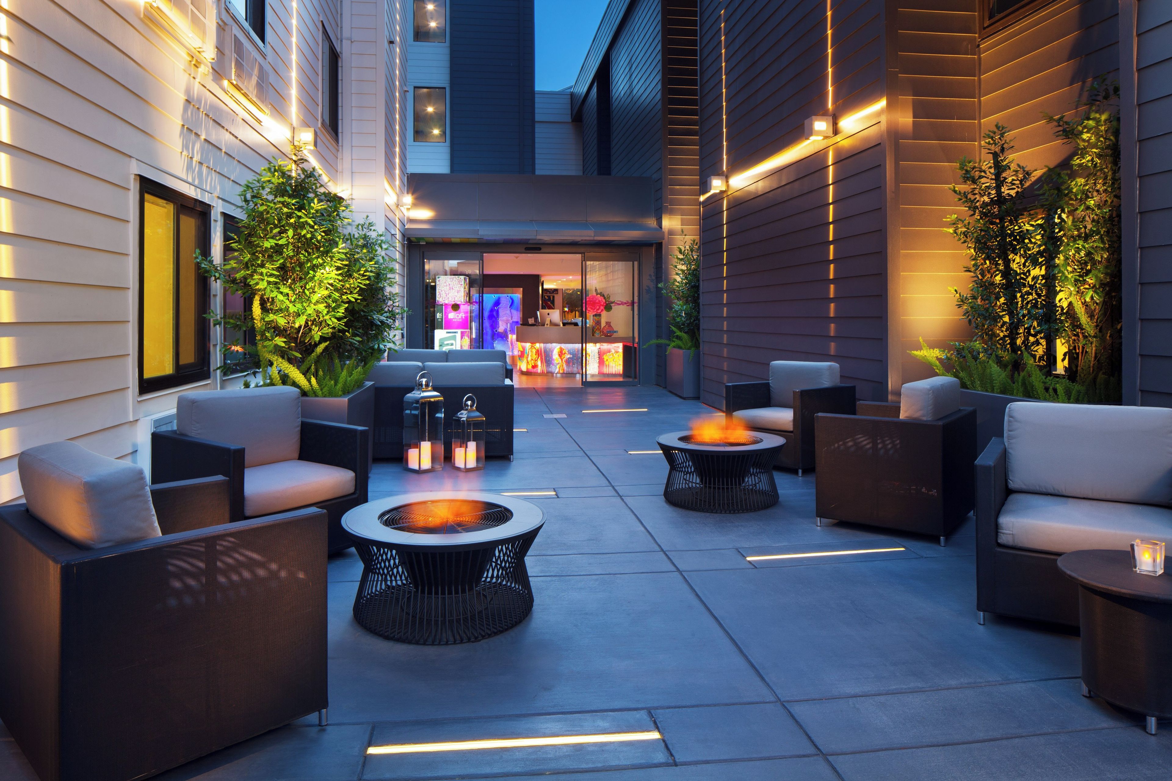 An outdoor seating area with fire pits and lounge chairs, surrounded by walls with integrated lighting.