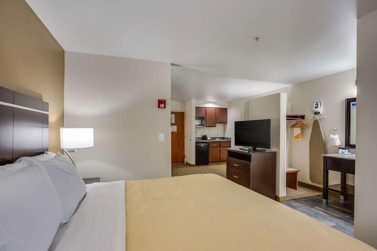 A hotel room with a bed, a desk, a television, a mirror, and a kitchenette.