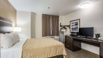A hotel room with a bed, a desk with a television, a coffee maker, and a picture frame on the wall.