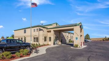 Un hotel con facciata beige, un'asta con la bandiera americana e un parcheggio con diverse automobili.