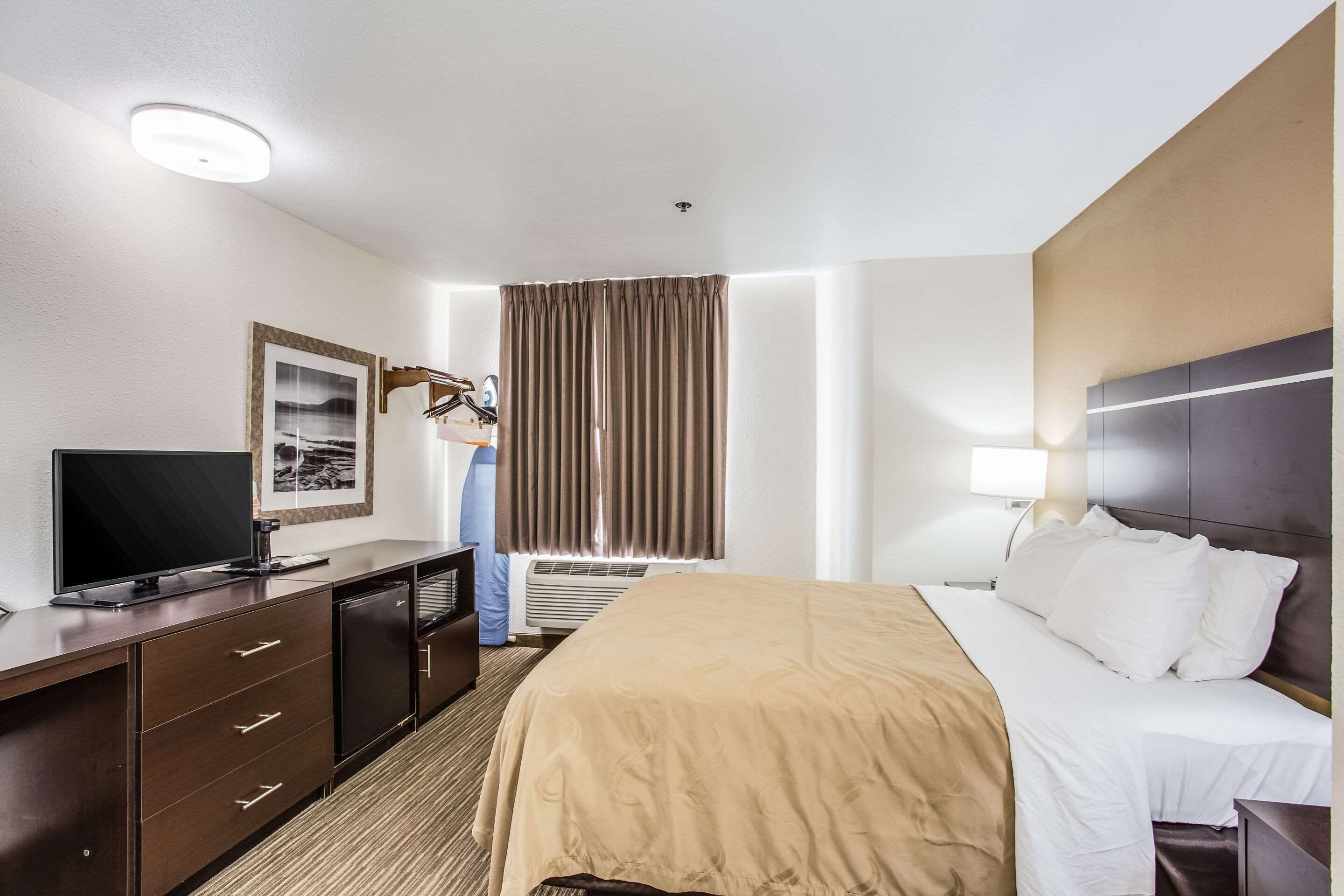 A hotel room with a bed, a TV, a dresser, and a window with curtains.