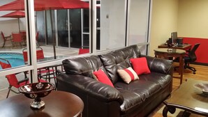 A living room with a black leather sofa, red cushions, a small table with a decorative bowl, and a view of a swimming pool through large windows. - FairBridge Inn Express Indianapolis South (Indianapolis)