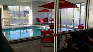 An indoor swimming pool with clear glass walls, red chairs, and umbrellas. - FairBridge Inn Express Indianapolis South (Indianapolis)
