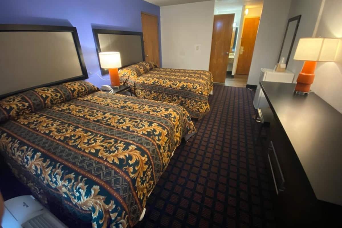 Une chambre d’hôtel avec deux lits, un bureau, un miroir et une lampe.