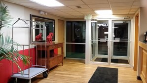 A reception area with a wooden desk, a red sofa, a plant, and a glass door leading outside. - FairBridge Inn Express Indianapolis South (Indianapolis)