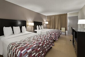 Een hotelkamer met twee bedden, elk met een ander beddegoed, een bureau met stoel en een groot raam met gordijnen.