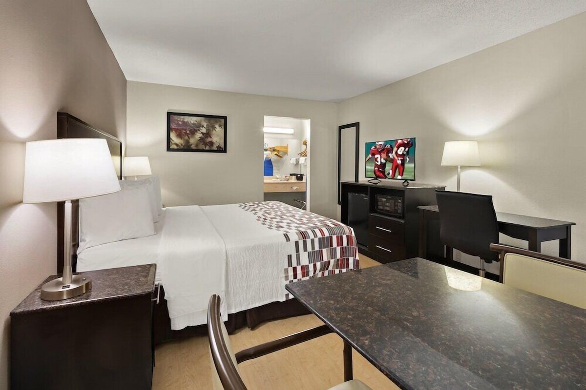 Een hotelkamer met een bed, bureau, stoel, televisie en een schilderij aan de muur.