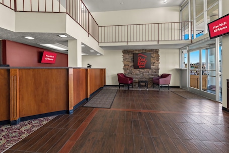 A hotel lobby with a reception desk, a stone wall with a logo, a staircase, and a seating area with chairs.