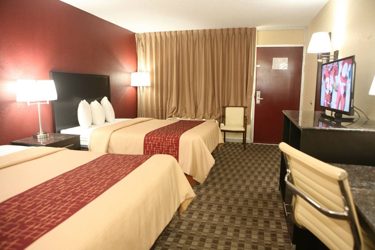 A hotel room with two beds, a desk with a television, a chair, and a lamp.