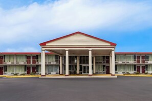 Un motel de dos pisos con entrada central, columnas y techo rojo.