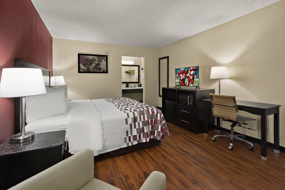 A hotel room with a bed, desk, chair, and a television.