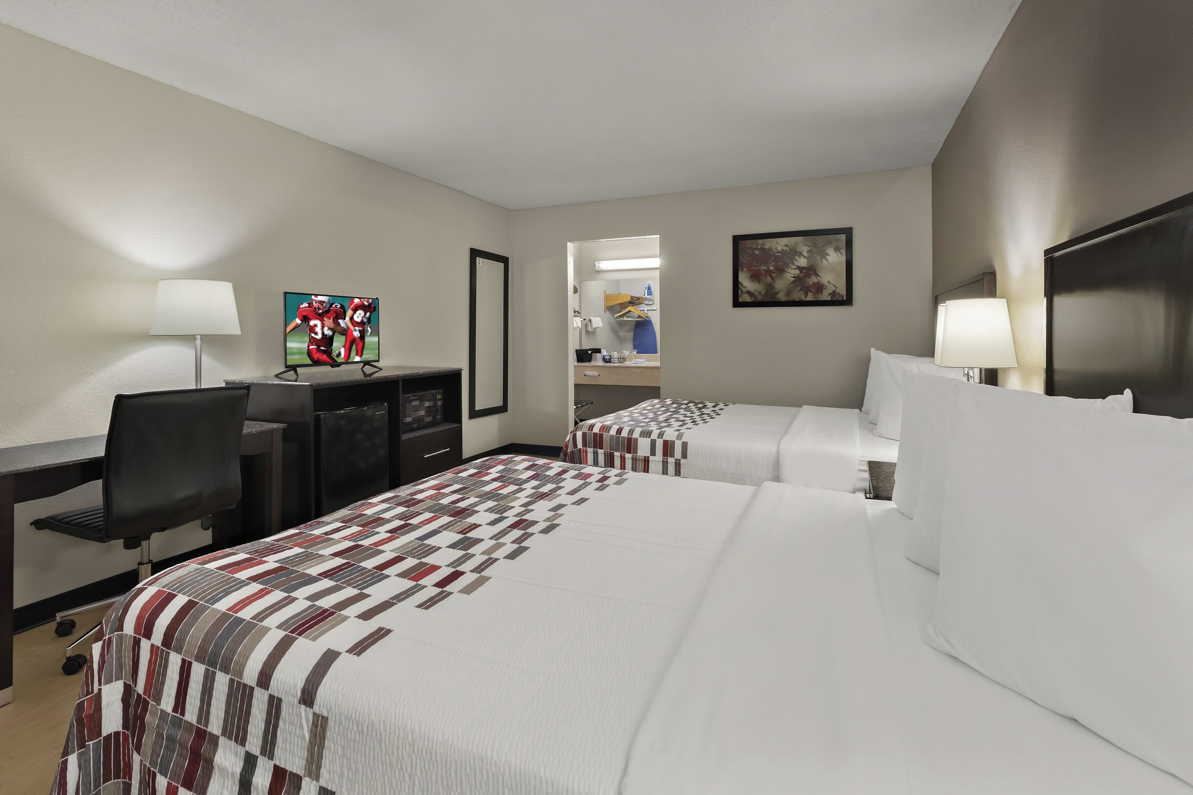 A hotel room with two beds, a desk with a computer, a TV, and a bathroom visible through an open door.