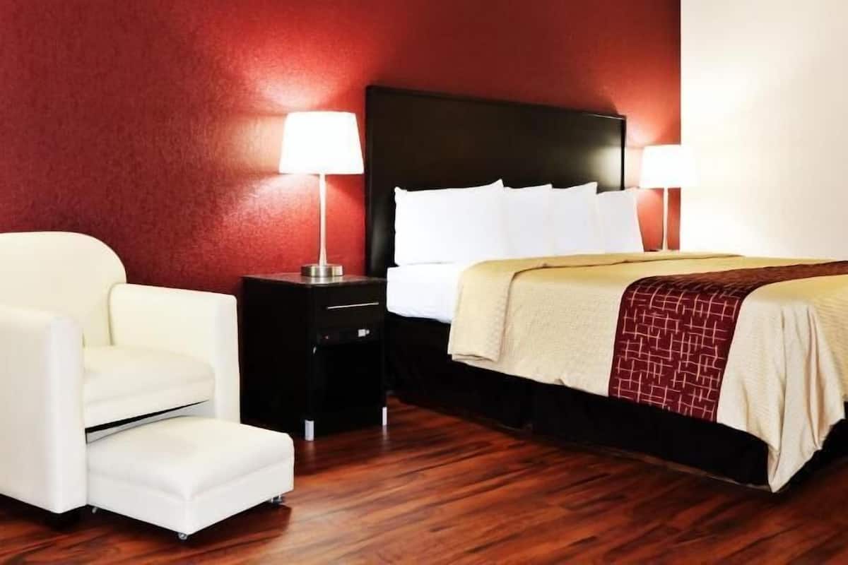 A hotel room with a bed, a chair, a nightstand, and a lamp.